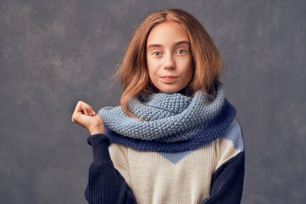 穿暖和毛衣的金发青少年女孩靠墙站立图片下载