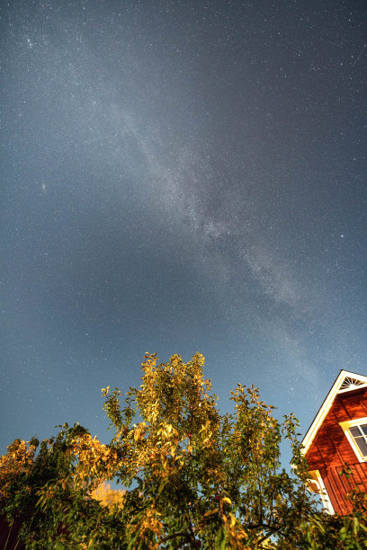 垂直照片银河星星在蓝色的天空上方的红色瑞典木屋和苹果树在夏末，秋天的花园图片下载