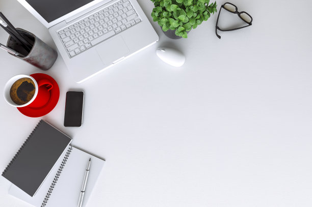 配有笔记本电脑的现代白色办公桌边，黑色屏幕的智能手机上方是一台笔记本电脑和一杯咖啡图片下载