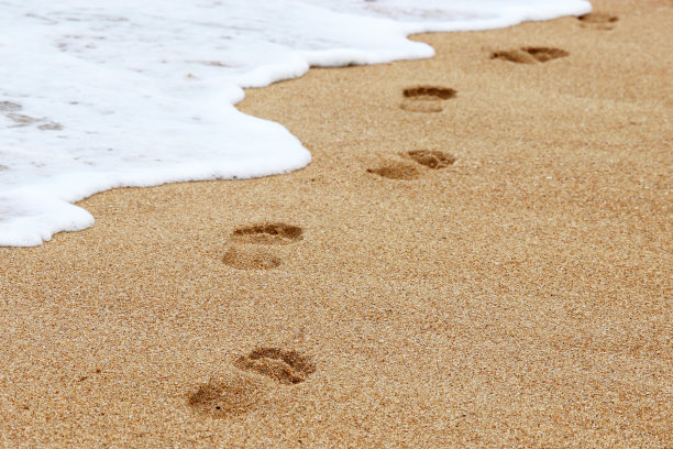 沙滩上裸露的脚印和海浪拍打海岸的泡沫图片下载