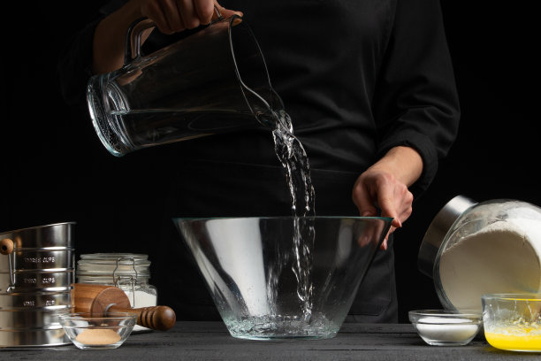 厨师为意大利面、披萨、面包和面包卷制作面团，将水倒进容器中，在运动中冻结。在黑色背景，水平照片图片下载