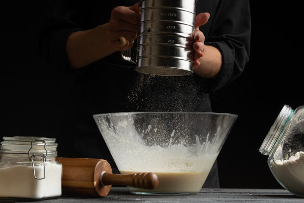 厨师准备好面团，将面粉倒入容器中，用于烘焙、面包、披萨或意大利面。在一张黑色背景的水平照片上静止不动图片下载