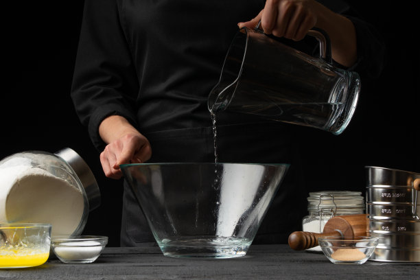 厨师为意大利面、披萨、面包和面包卷制作面团，将水倒进容器中，在运动中冻结。在黑色背景，水平照片图片下载