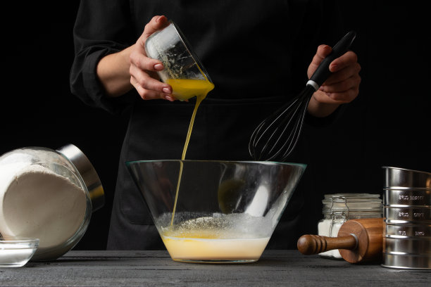 糕点师或面包师烹饪面团，把酵母倒进容器里，用来制作糖果、面包卷、意大利披萨或意大利面。冻结。在黑色背景，水平照片图片下载