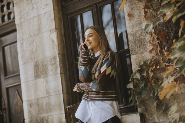 秋日，一个漂亮的年轻女子拿着手机站在街上图片下载