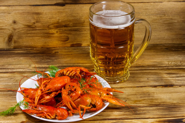 木桌上放着煮小龙虾和一大杯啤酒图片下载