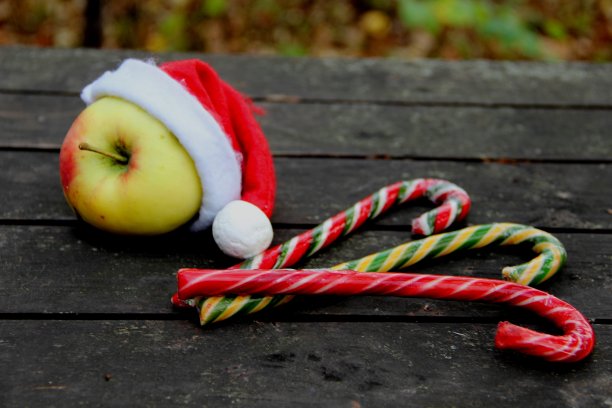 一个戴着圣诞老人帽子的苹果，三根彩色的焦糖手杖。圣诞老人帽，深棕色背景上的三根棒棒糖图片下载