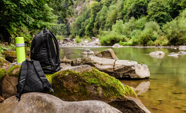 旅行背包和保温瓶站在森林河岩石上图片下载