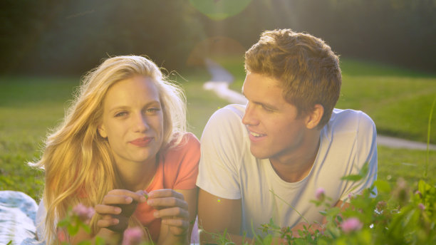 照片:一对年轻的学生夫妇躺在宁静的草地上打电话回家。图片下载