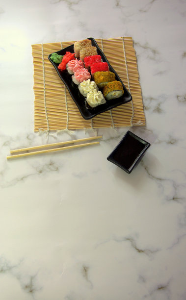 寿司放在一个黑色的平盘子上，在一张竹餐巾上，还有筷子和一个盛有酱油的杯子。图片下载