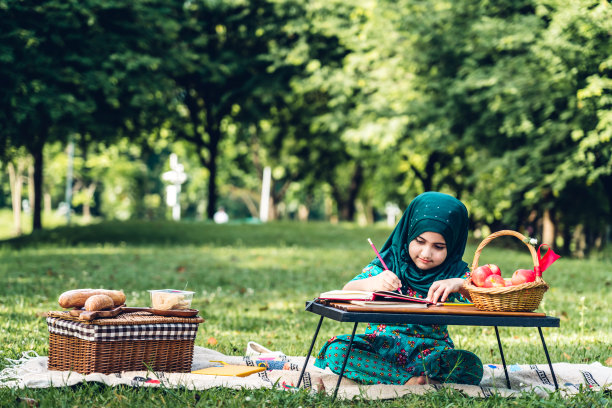 快乐的小穆斯林女孩的肖像，穿着头巾的孩子微笑着享受放松的阅读和写在夏天的公园里的书。教育的概念图片下载