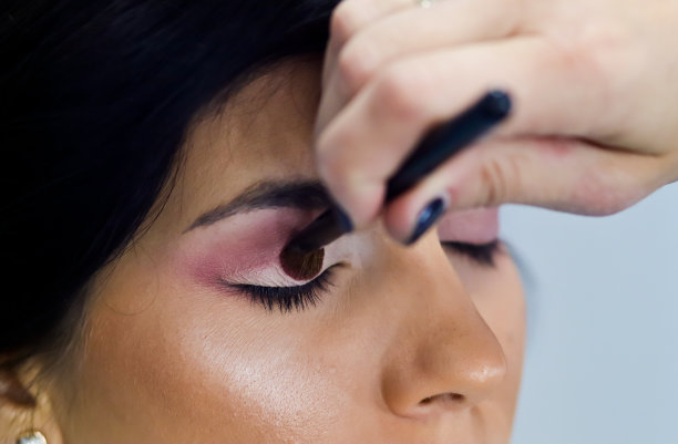 粉妆艺术家用刷子在模特眼睛上工作近距离应用粉红色眼影在年轻女孩闭上眼睛。图片下载