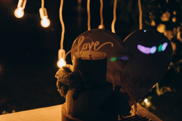 婚礼蛋糕装饰鲜花和巧克力字“爱”的背景与灯光婚礼拱门访问仪式。选择性对焦，胶片和颗粒照片图片下载