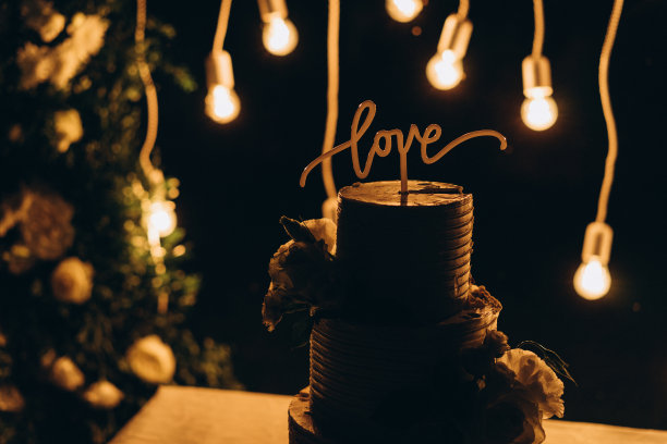婚礼蛋糕装饰鲜花和巧克力字“爱”的背景与灯光婚礼拱门访问仪式。选择性对焦，胶片和颗粒照片图片下载