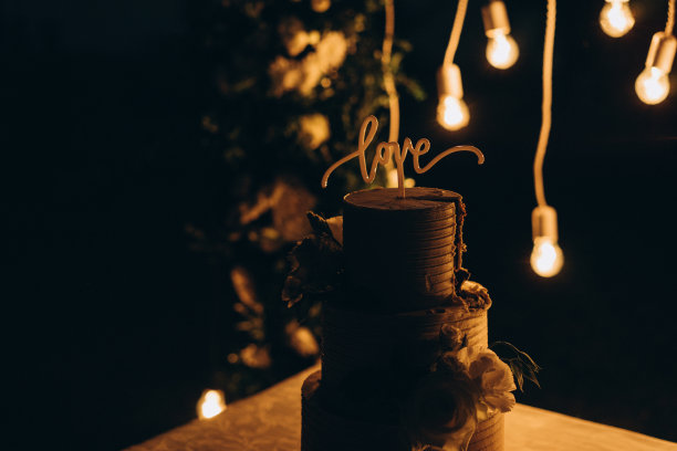 婚礼蛋糕装饰鲜花和巧克力字“爱”的背景与灯光婚礼拱门访问仪式。选择性对焦，胶片和颗粒照片图片下载