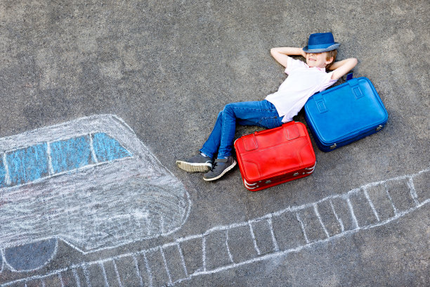 小男孩在沥青上用彩色粉笔画高速列车图片。孩子们用粉笔和蜡笔画画，去度假。学生坐在手提箱上。图片下载