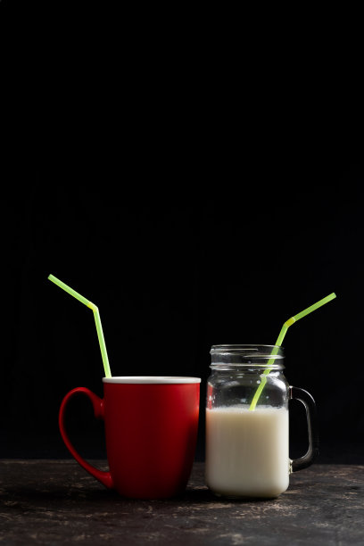 红色杯和玻璃杯，牛奶和黄色吸管在黑色的背景。本空间图片下载