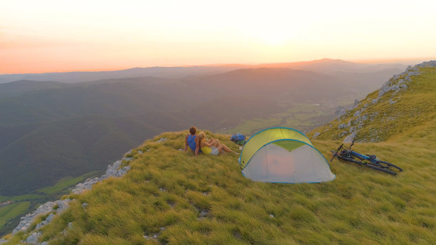 图片:日落时分，一对骑山地车的情侣在帐篷旁拥抱。图片下载