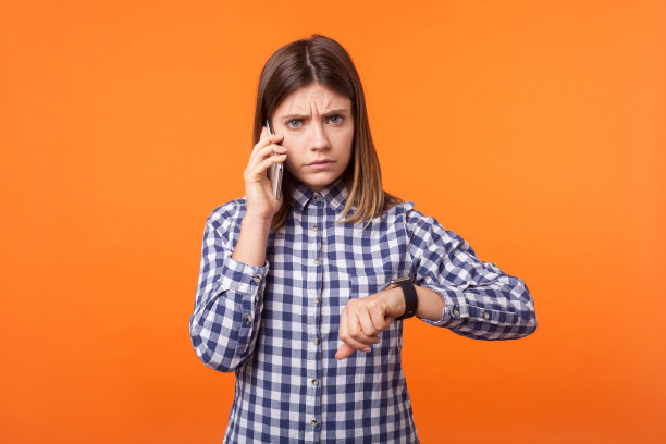 一幅心烦意乱的年轻女子的肖像，棕色头发，穿着格子衬衫，正在打电话。室内工作室拍摄孤立的橙色背景图片下载