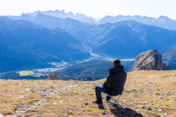 一个男人坐在露营椅上，背景是一个美丽的高山山谷。图片下载