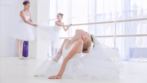 芭蕾舞课上，身穿白色芭蕾舞裙的女童正在做伸展运动图片下载