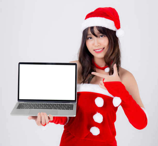 美丽的年轻亚洲女人在圣诞老人呈现笔记本电脑在圣诞假期孤立的白色背景，亚洲女孩显示笔记本和指向庆祝在圣诞节或新年。图片下载