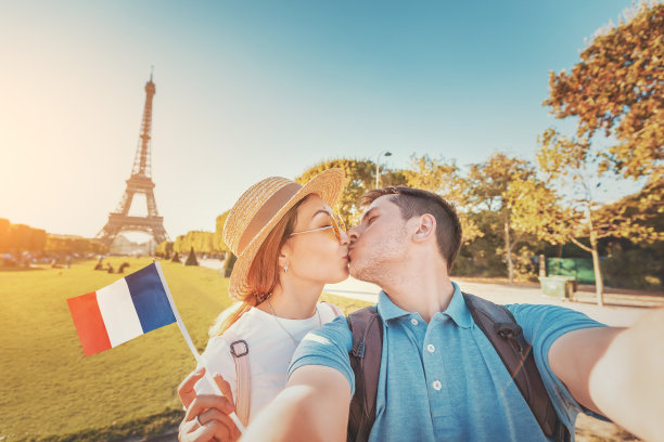 这对混血儿以法国国旗和埃菲尔铁塔为背景，互相拥抱自拍。蜜月旅行在法国和巴黎的概念图片下载