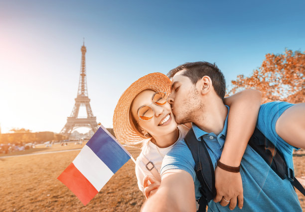 这对混血儿以法国国旗和埃菲尔铁塔为背景，互相拥抱自拍。蜜月旅行在法国和巴黎的概念图片下载
