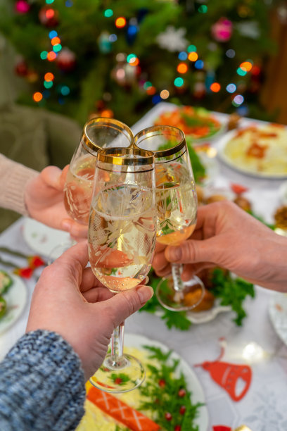 人的手拿着起泡酒的杯子。朋友或家人对着圣诞餐桌和装饰好的新年树举杯畅饮。在温馨的家中庆祝寒假图片下载