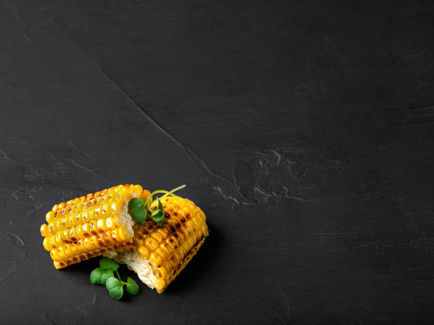 烤过的黄色玉米棒子和绿色芽在黑色的背景。特写镜头。前视图。本空间图片下载