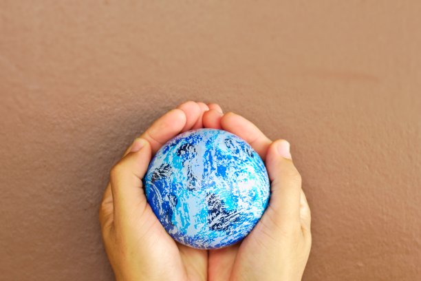 棕褐色墙壁背景上的一个小地球仪。蓝色小世界双手棕色墙壁背景上方自由空间四周。本空间图片下载