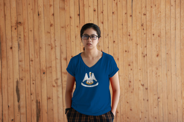 一名女子穿着路易斯安那州国旗色衬衫，双手插在裤子口袋里，站在木墙背景上。图片下载