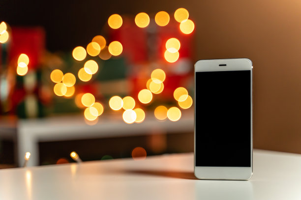 白色桌子上的智能手机，散焦圣诞灯和圣诞礼物的背景，散焦图片下载