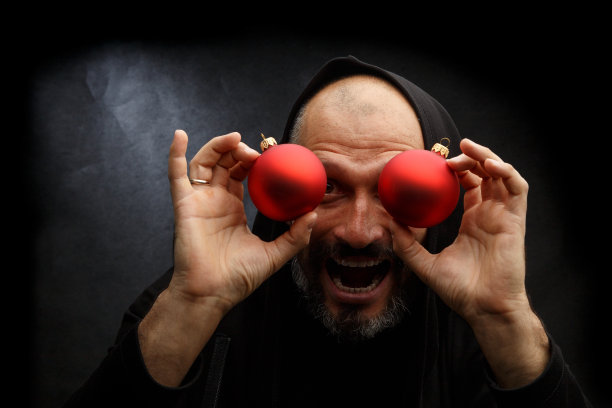 一个戴着黑色头巾留着胡子的秃顶男人的肖像，在肮脏的灰色背景上有一个红色的圣诞球。年轻的圣诞老人的概念。图片下载