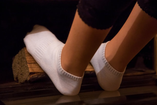 一个女孩在烧木头的炉子里温暖她的双腿。图片下载