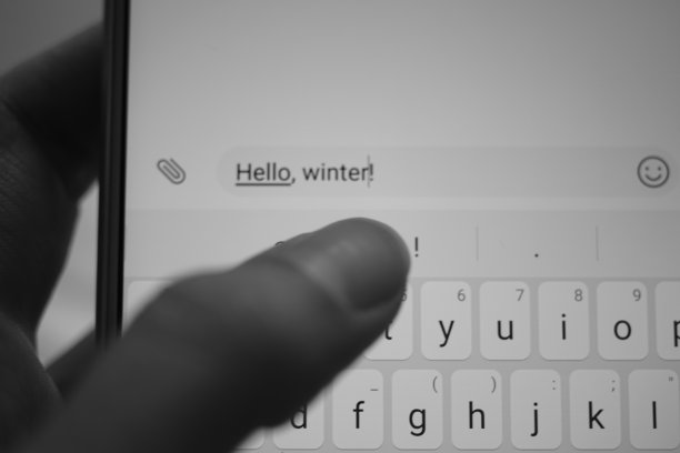 女性在白色智能手机上输入一条信息:你好，冬天。黑白照片。图片下载