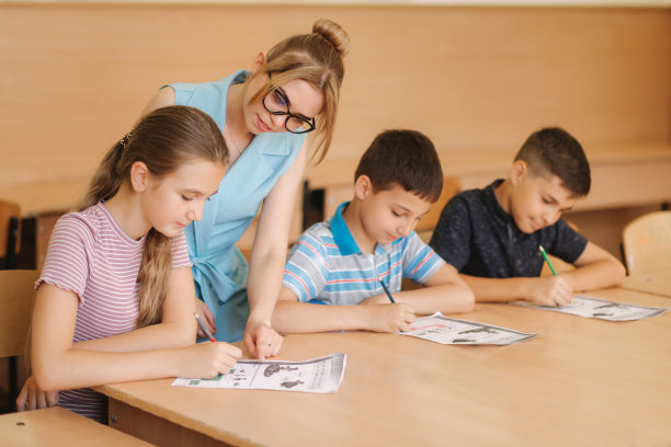 老师在课堂上帮助学生写作。教育，小学，学习和人的观念图片下载