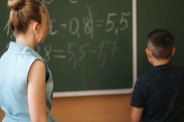 年轻女教师帮助男生。男孩站在黑板旁边图片下载