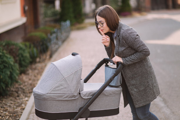 年轻的妈妈推着婴儿车走着把手指放在嘴唇上说嘘。妈妈一边沉默图片下载