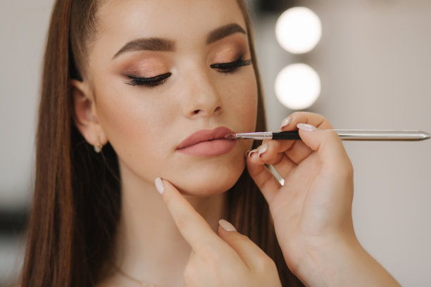 化妆师涂口红。化妆师手，画着年轻美女红发模特嘴唇。在过程中弥补。特写视图图片下载