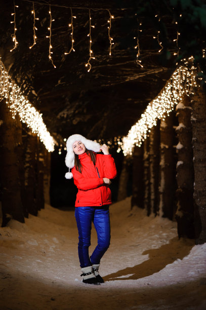 户外照片年轻美丽的快乐微笑的女孩，摆姿势在装饰着灯泡的小巷。圣诞集市的背景。图片下载