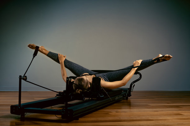 小女孩在床上做普拉提练习。美丽苗条的健身教练对改革者灰色背景，低调，艺术光。健康的概念图片下载