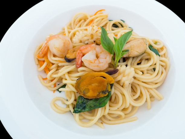 辛辣的意大利面和海鲜放在一个白色的盘子上，孤立在黑色的背景上图片下载