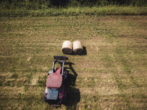 空中从上到下的无人机照片的农民收割干草卷在麦田与一辆红色拖拉机图片下载