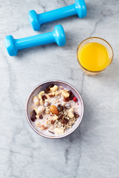 一碗加了酸奶、坚果、葡萄干、蔓越莓和奇亚籽的格兰诺拉麦片。背景是蓝色的哑铃。一个美味和健康的概念。石头的背景。前视图。副本的空间。图片下载