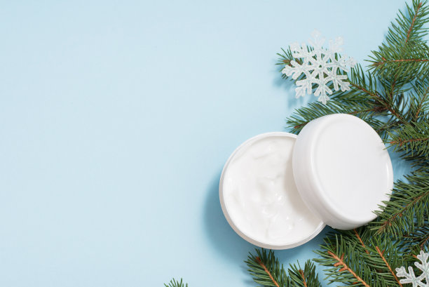 白色奶油与圣诞树和雪花在蓝色背景，复制空间。冬天身体保健图片下载