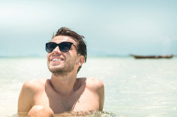 年轻英俊的男人戴着太阳镜在蔚蓝的大海里晒太阳。暑假的概念图片下载