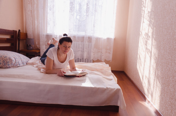 一个快乐的年轻女人在家里看书。图片下载