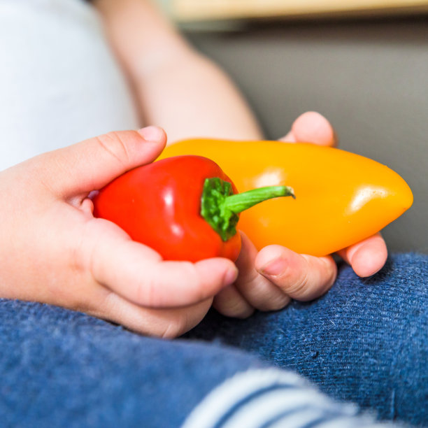 男婴手捧生鲜红黄辣椒室内。婴儿探索蔬菜图片下载