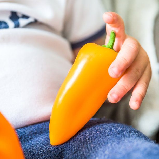 男婴手捧生鲜红黄辣椒室内。婴儿探索蔬菜图片下载